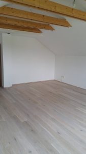 Dřevěná podlaha Dub bělený kartáčovaný – White Plains v obývacím pokoji rodinného domku. Povrch je ošetřený vodě a…